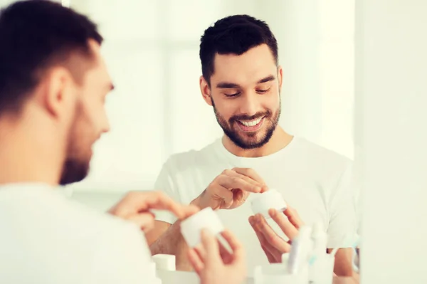 Happy young man applying cream to face at bathroom — Stock Photo, Image