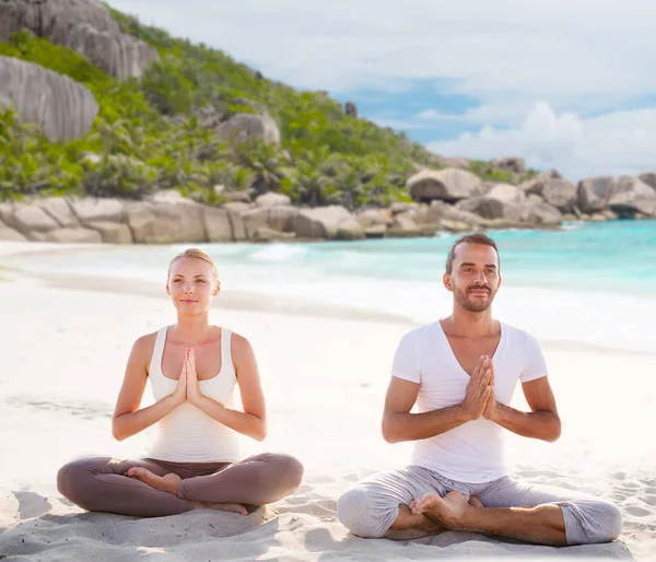 Coppia sorridente fare esercizi di yoga sulla spiaggia — Foto Stock
