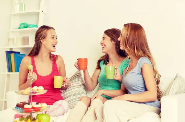 Mujeres jóvenes felices bebiendo té con dulces en casa —  Fotos de Stock