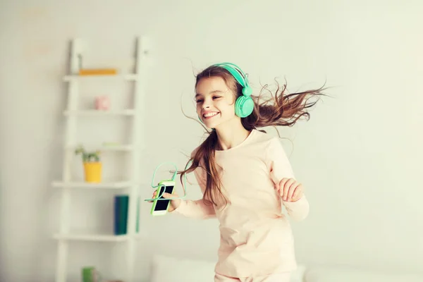 Girl jumping on bed with smartphone and headphones — Stock Photo, Image