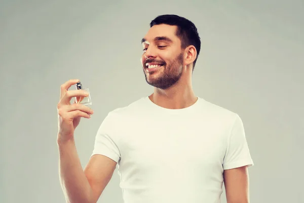 Hombre sonriente con perfume masculino sobre fondo gris —  Fotos de Stock