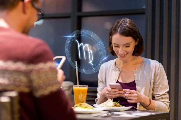 Pareja con teléfonos inteligentes y signos del zodiaco en la cafetería —  Fotos de Stock