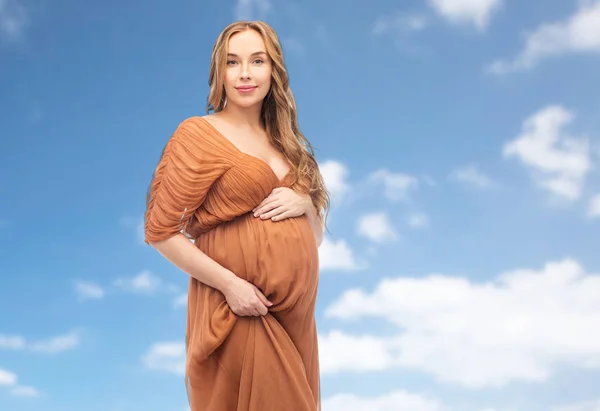 Happy pregnant woman touching her belly over sky — Stock Photo, Image