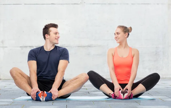Glada sportiga mannen och kvinnan sitter på mattor — Stockfoto