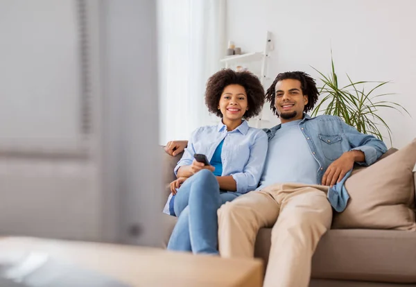 Sonriente pareja con control remoto viendo tv en casa —  Fotos de Stock