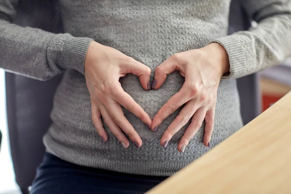 Mulher grávida fazendo forma de coração no escritório — Fotografia de Stock