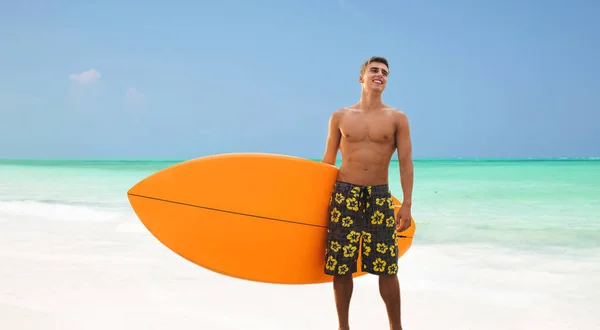 Jovem sorridente com prancha de surf na praia — Fotografia de Stock