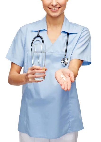 Улыбающийся врач или медсестра предлагает таблетки и воду — стоковое фото