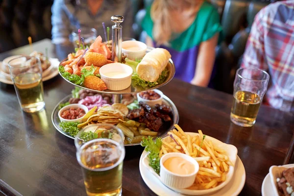 Pessoas sentadas à mesa com comida e cerveja no bar — Fotografia de Stock