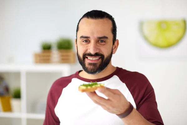 Человек ест бутерброды с авокадо на домашней кухне — стоковое фото