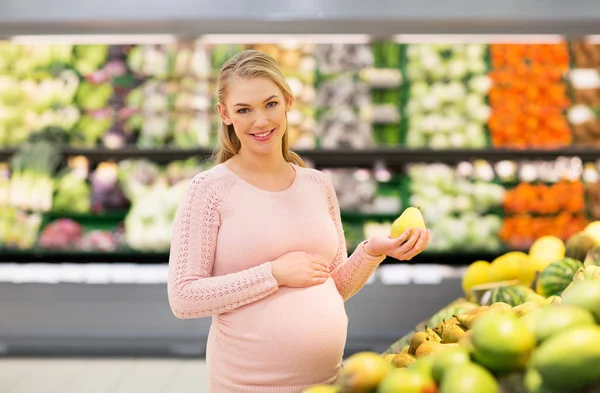 Mujer embarazada feliz con pera en la tienda de comestibles — Foto de Stock