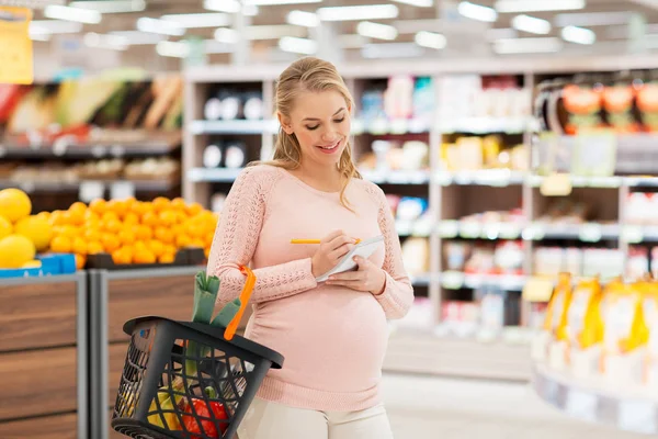 Pregnant woman with shopping basket at grocery — Stock Photo, Image