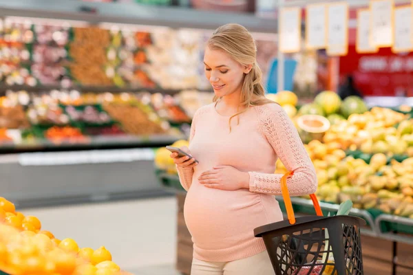 Mujer embarazada con cesta de la compra y smartphone — Foto de Stock