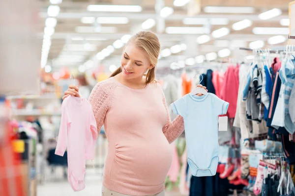 Gravid kvinna med babykläder på kläder förvaras — Stockfoto