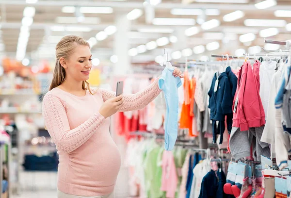 Mujer embarazada tomando fotos de ropa de bebé —  Fotos de Stock