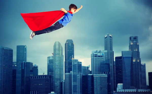 Niño en capa de superhéroe rojo volando sobre la ciudad — Foto de Stock