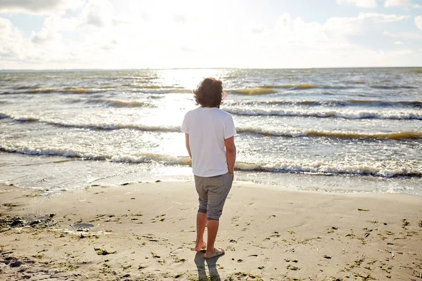 Молодой человек на летнем пляже смотрит на море — стоковое фото