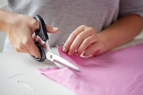 woman with tailor scissors cutting out fabric