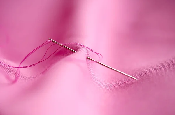 Aguja de coser con hilo pegado en tela rosa — Foto de Stock