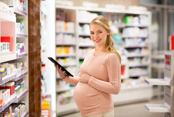 Счастливая беременная женщина с планшетным ПК в аптеке — стоковое фото