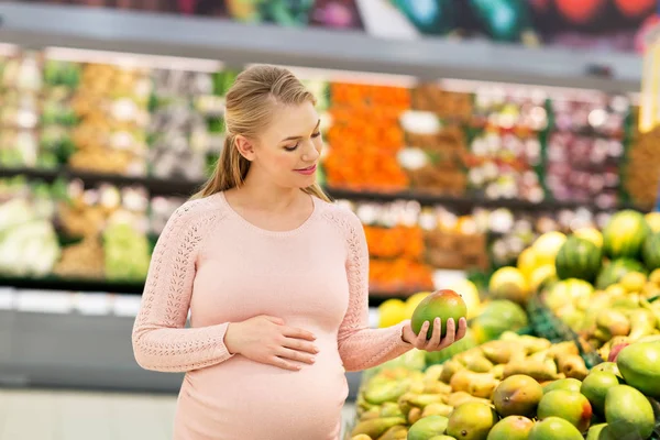 Szczęśliwy w ciąży kobieta z mango w sklepie spożywczym — Zdjęcie stockowe