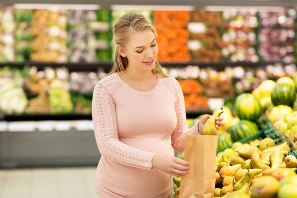 Mulher grávida com saco comprando pêras no supermercado — Fotografia de Stock