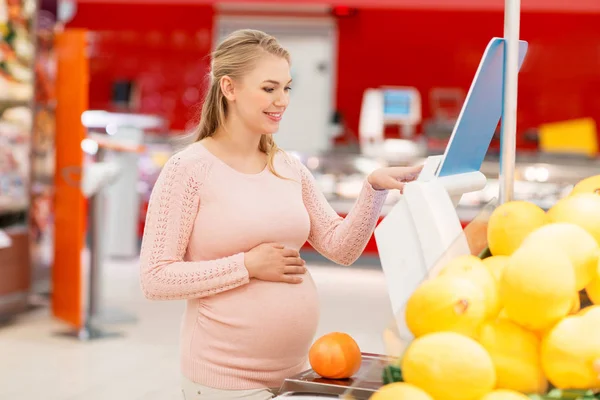 Mulher grávida com toranja em escala no supermercado — Fotografia de Stock