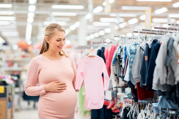 Mulher grávida com roupas de bebê na loja de roupas — Fotografia de Stock