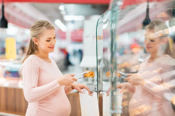 Беременная женщина с сумкой покупает булочки в продуктовом — стоковое фото