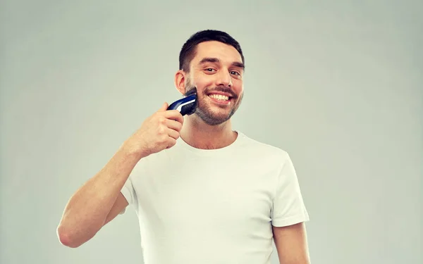 Sonriente hombre afeitando la barba con trimmer sobre gris —  Fotos de Stock