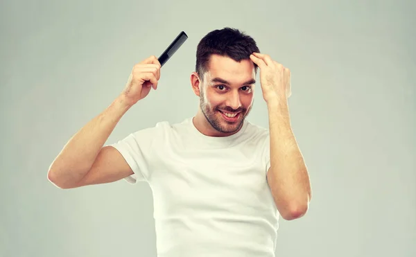 Hombre feliz cepillando el cabello con peine sobre gris — Foto de Stock