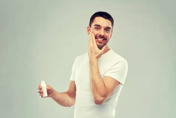 Felice giovane uomo applicando crema o lozione per il viso — Foto Stock