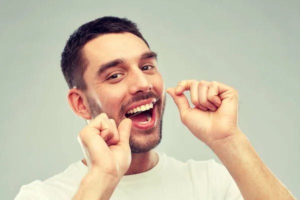 Hombre con hilo dental limpieza de dientes sobre gris — Foto de Stock