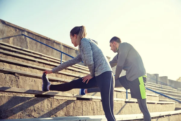 Couple stretching leg on stands of stadium — Stock Photo, Image