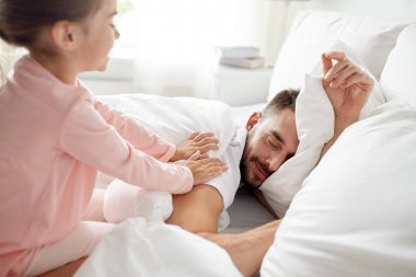 little girl waking her sleeping father up in bed clipart