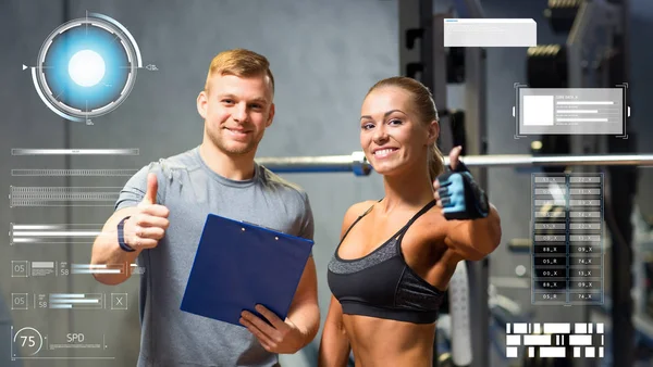 Sorrindo jovem mulher com personal trainer no ginásio — Fotografia de Stock