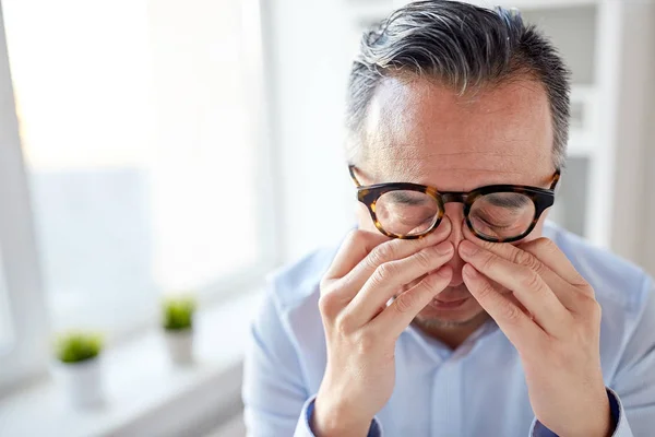 Businessman in glasses rubbing eyes at office — Stock Photo, Image