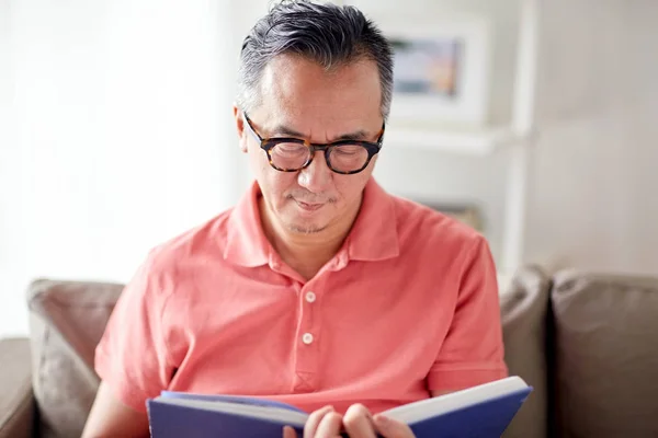Мужчина сидит на диване и читает книгу дома — стоковое фото