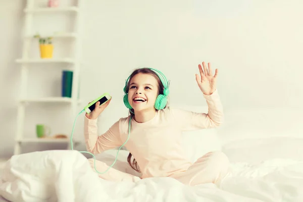 Mädchen sitzt mit Smartphone und Kopfhörer im Bett — Stockfoto