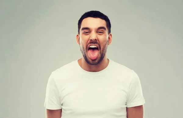 Muž ukazuje svůj jazyk přes šedé pozadí — Stock fotografie