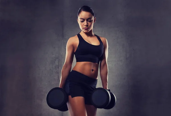 Молодая женщина сгибает мышцы гантелями в спортзале — стоковое фото