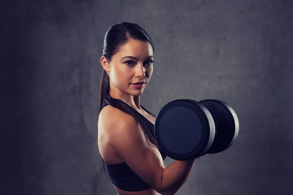 Mujer joven flexionando los músculos con pesas en el gimnasio — Foto de Stock