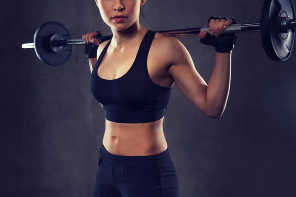 Mujer joven flexionando los músculos con barra en el gimnasio —  Fotos de Stock