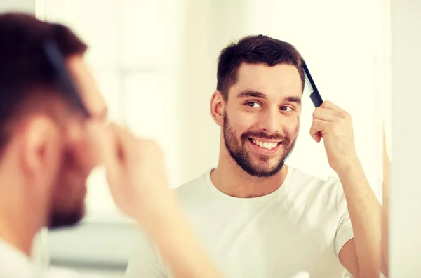 Homem feliz escovando o cabelo com pente no banheiro — Fotografia de Stock