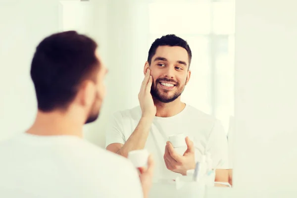 Щасливий молодий чоловік наносить крем обличчям у ванній — стокове фото