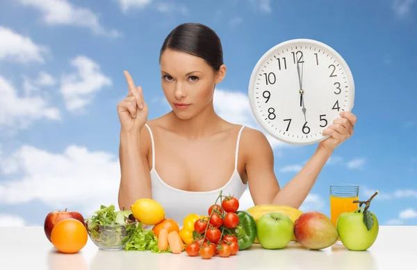 Femme avec de la nourriture et une grande horloge assise à table — Photo