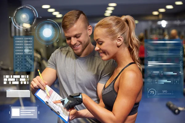 Smiling woman with trainer and clipboard in gym — Stock Photo, Image