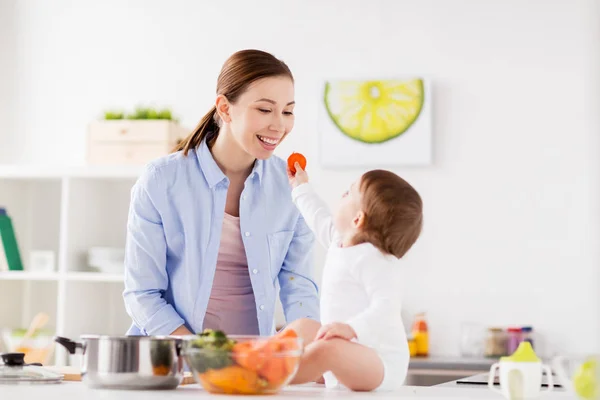 Bébé nourrissant mère avec carotte à la maison cuisine — Photo