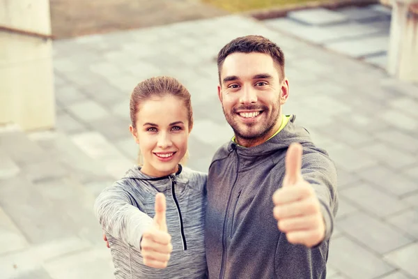 Sonriente pareja mostrando pulgares en la calle de la ciudad — Foto de Stock