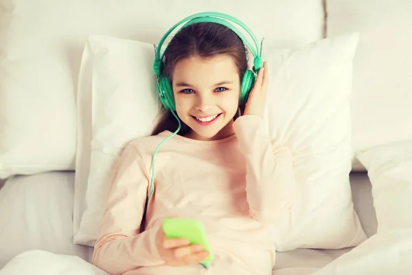 Lykkelig jente som ligger i senga med smarttelefonen hjemme – stockfoto
